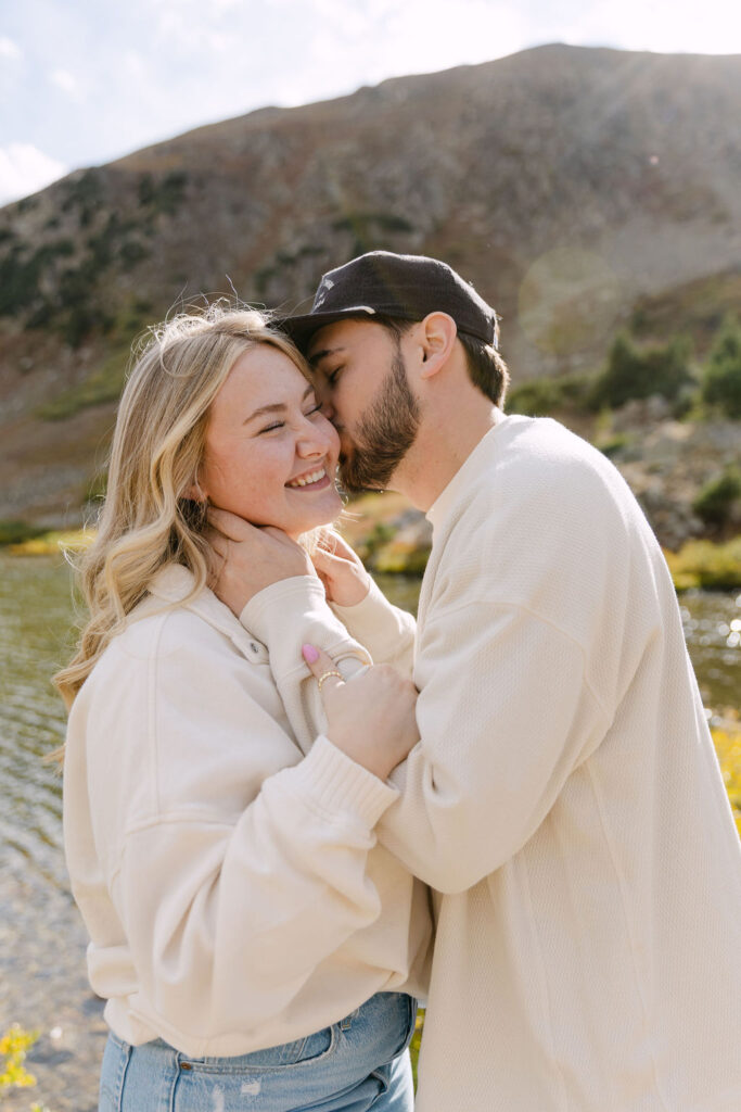 Girl smiling as her fiance kisses her on the cheek at Loveland Pass
