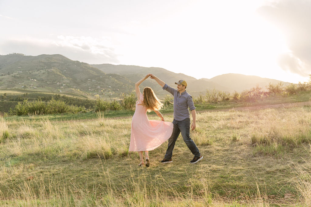 Couple slow dancing in a sunlit field with the foothills behind them.
