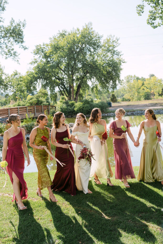 Bride walking with bridesmaids in jewel-tone dresses at Hudson Gardens, a luxury Colorado garden wedding venue.