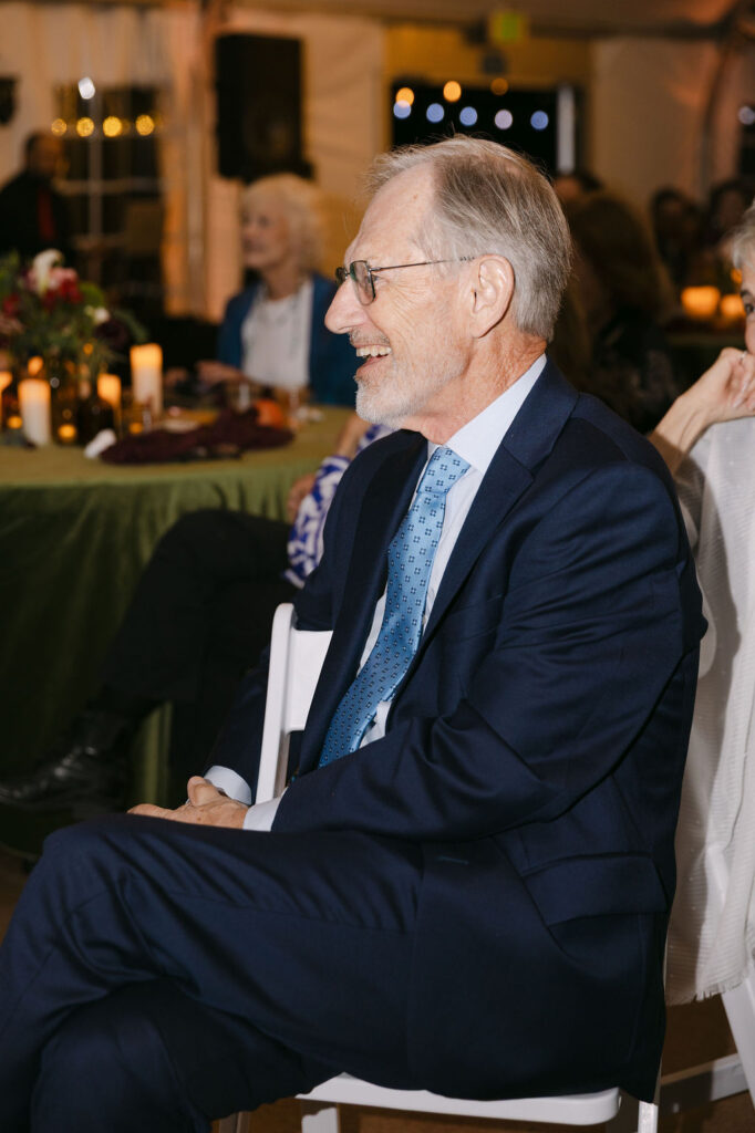 Wedding guest smiling during heartfelt speeches in a luxury tented reception at Hudson Gardens.