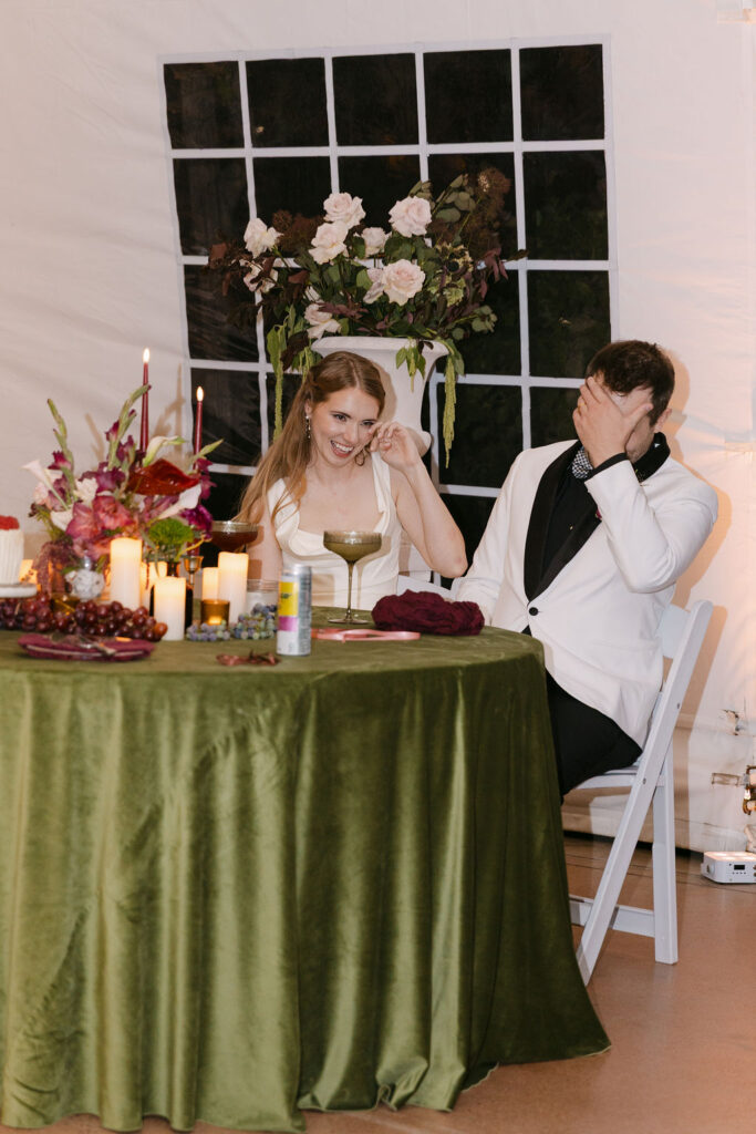 Bride and groom seated together laughing during reception speeches at Hudson Gardens.