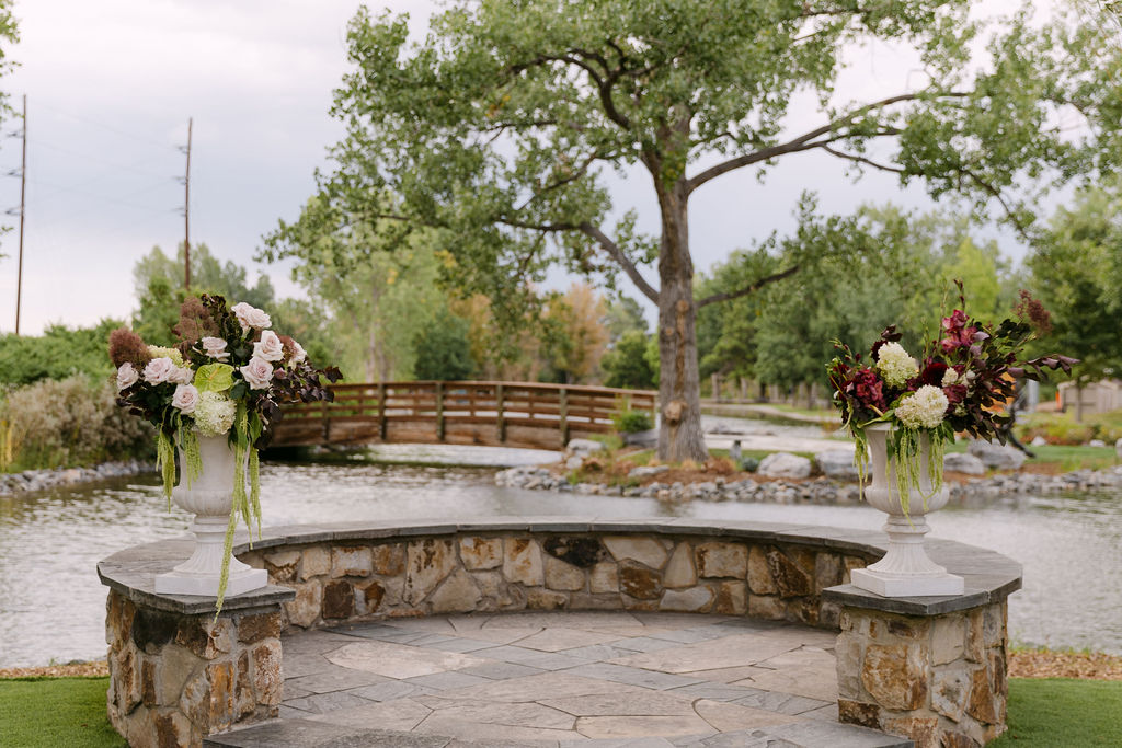 Ceremony site setup at Hudson Gardens with stone wall and lush floral urns for a luxury Colorado outdoor wedding.