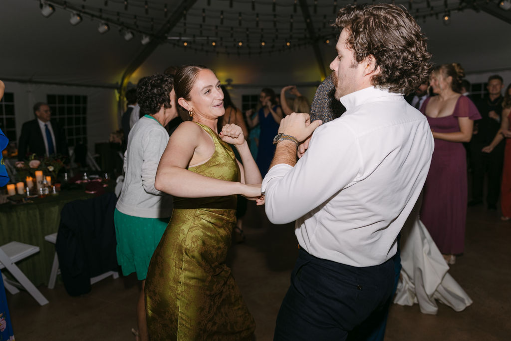 Bridesmaid in olive green dress dancing with a guest during an upscale Hudson Gardens wedding reception.