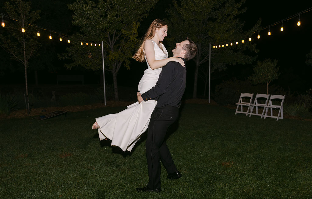 Groom lifting the bride during a romantic nighttime dance at an outdoor Colorado wedding reception.