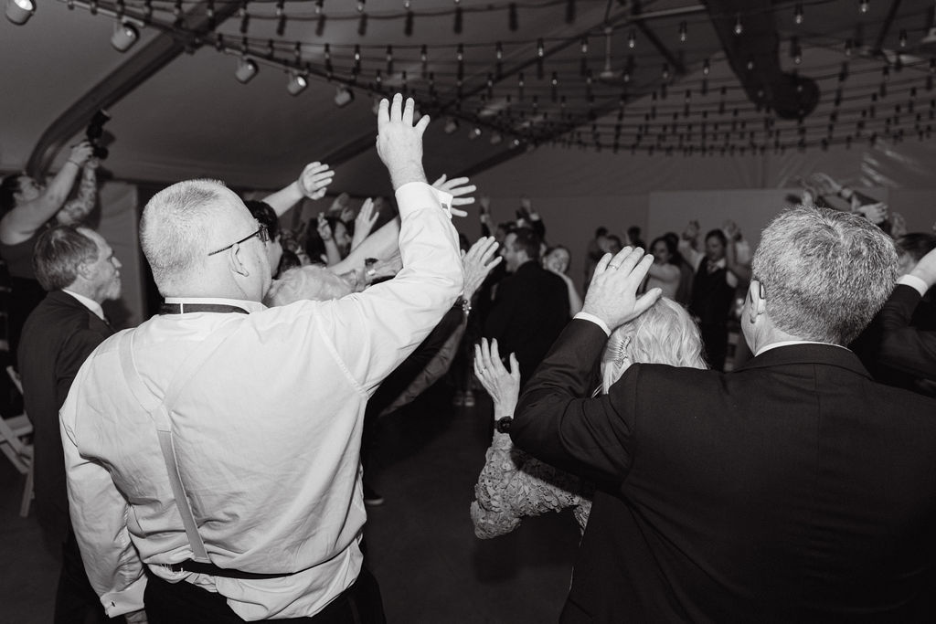Black-and-white image of guests cheering and dancing at a packed Hudson Gardens wedding reception.