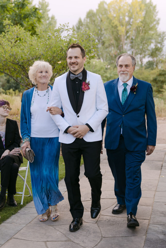 Groom walking down the aisle with parents during a Hudson Gardens ceremony in Littleton, Colorado.