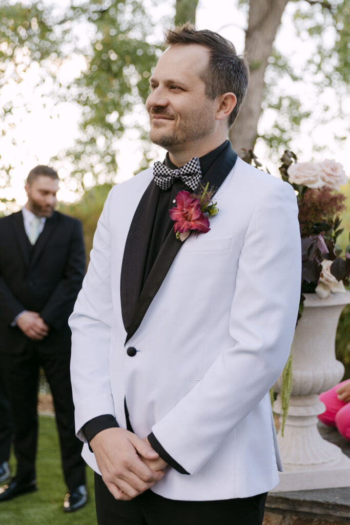 Groom waiting at the altar in a white tuxedo during a luxury garden wedding at Hudson Gardens in Colorado.