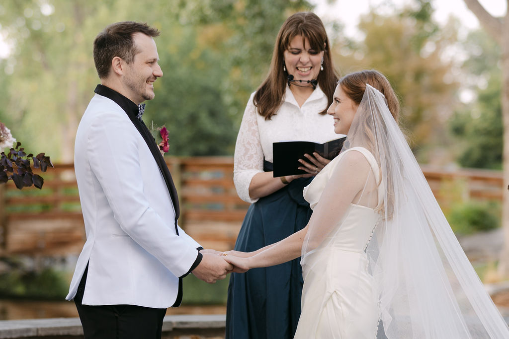 Bride and groom holding hands during vows at their Colorado garden wedding.