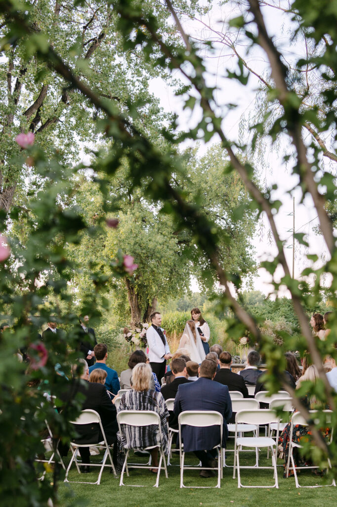 Outdoor ceremony at Hudson Gardens, a Colorado garden wedding venue, photographed through lush greenery for a luxury fine-art wedding look.