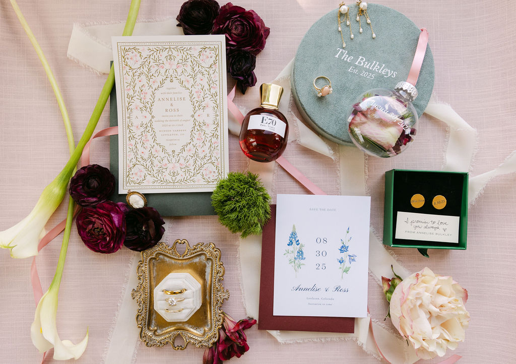 Flatlay of luxury wedding details with invitation suite, perfume bottle, florals, and heirloom pieces for an elegant Colorado wedding.
