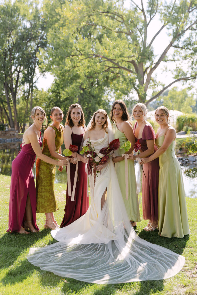 Bridesmaids in mismatched jewel-tone dresses posing with the bride at Hudson Gardens, a high-end Colorado garden wedding venue.
