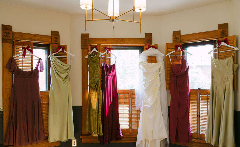 Bridesmaid dresses and wedding gown hanging in a bright room before a Hudson Gardens wedding in Littleton, Colorado.