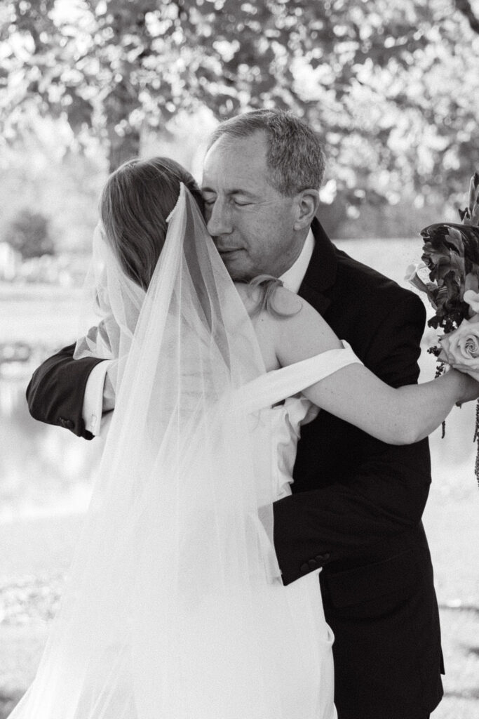 Black-and-white candid of bride hugging her father during a heartfelt moment at a Colorado wedding ceremony.