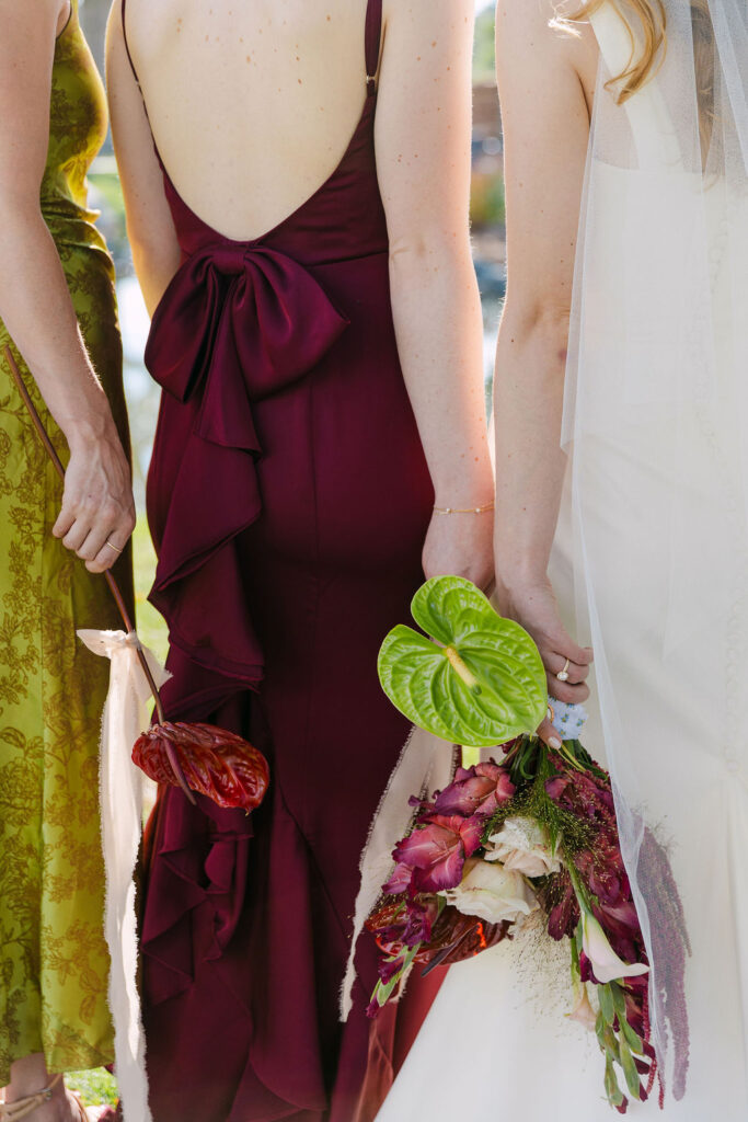 Back view of bridesmaid in deep burgundy dress holding tropical-inspired bouquet at a Colorado garden wedding.