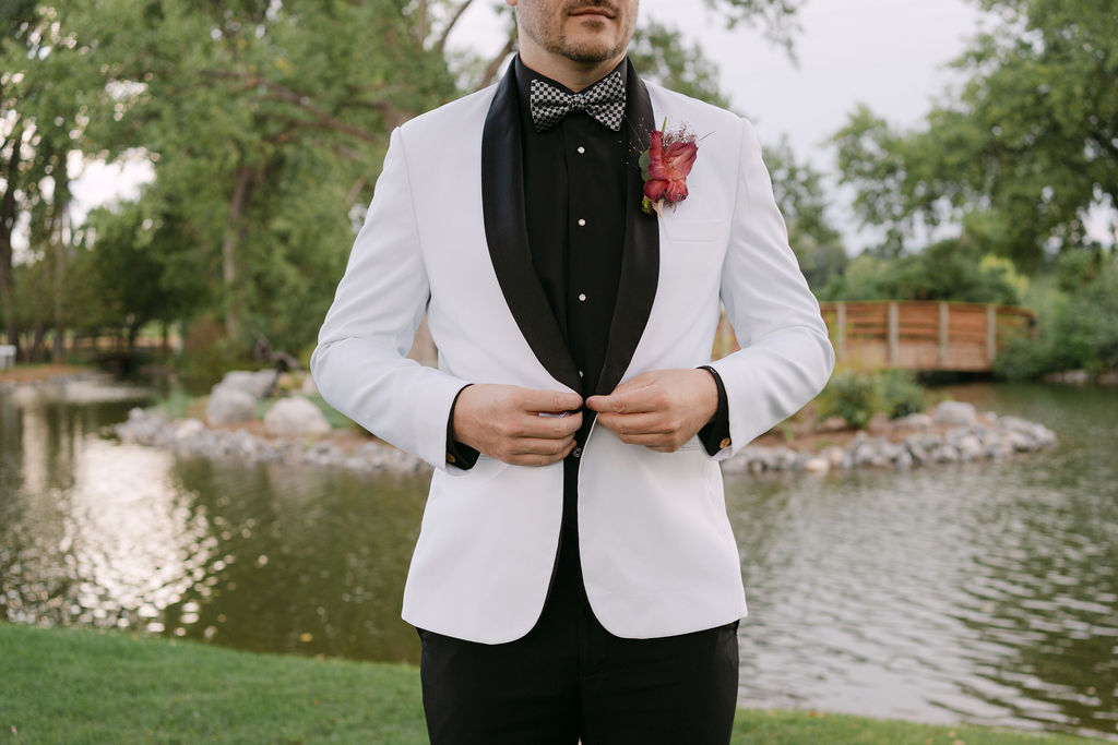 Groom adjusting white tuxedo jacket with black lapels, preparing for an upscale Hudson Gardens wedding.