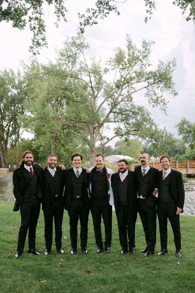 Groomsmen in classic black suits posing outdoors at Hudson Gardens for a luxury Colorado wedding.