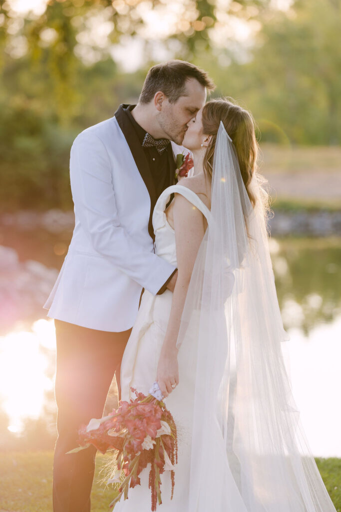 Romantic golden-hour kiss by the pond at Hudson Gardens, featuring luxury Colorado wedding photography.