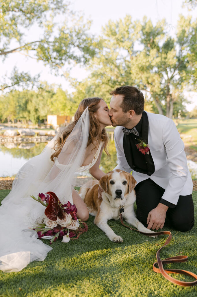 Bride and groom kissing with their dog at Hudson Gardens during a Colorado garden wedding, captured in natural, romantic light.