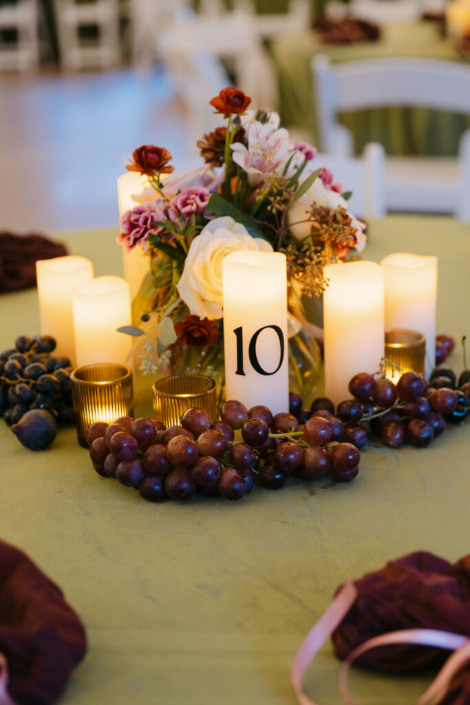 Romantic candlelit centerpiece with grapes, florals, and table number at an elegant Colorado garden wedding reception.