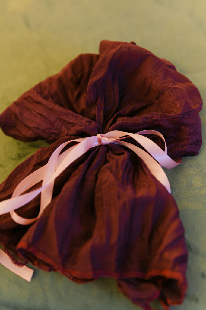 Maroon silk napkin with ribbon tie on green velvet tablecloth at a luxury Colorado wedding.
