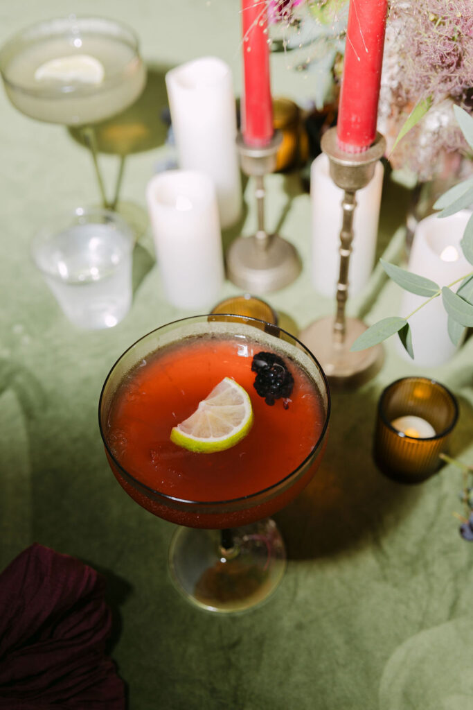 Signature cocktail with blackberry garnish on green velvet linen at a luxury Hudson Gardens wedding reception.