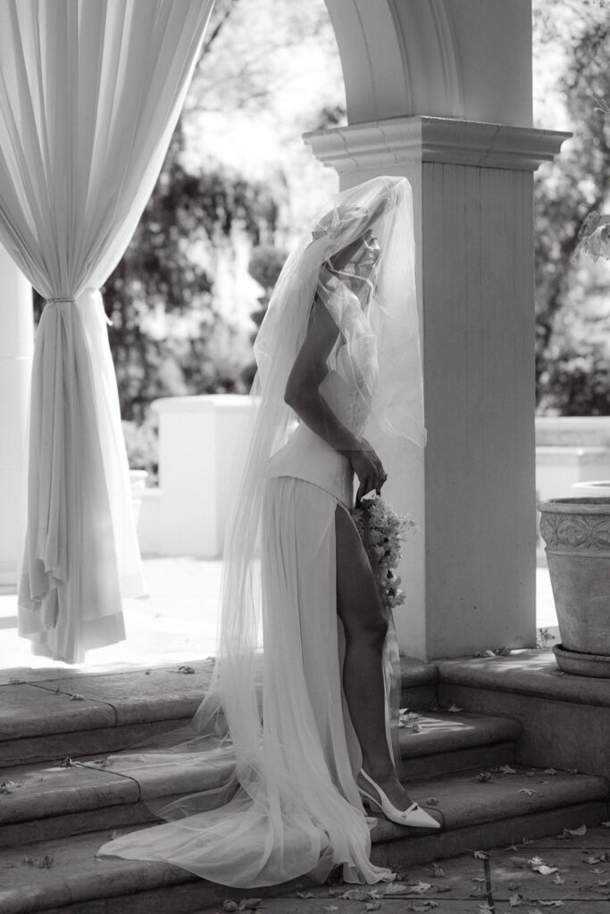 Editorial bridal portrait with a romantic, cathedral length veil and large bridal sun hat on the steps of Oceana's Gardens under italian-inspired architecture 