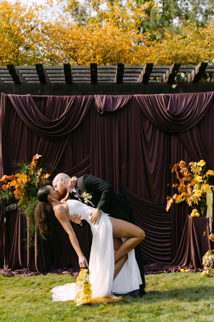 First kiss at a wedding ceremony held at Oceana's Gardens wedding venue in Colorado against a luxury drapery backdrop 
