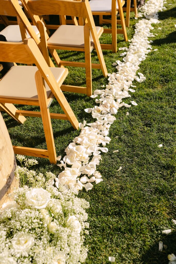 Petal-lined ceremony aisle with wooden chairs at a high-end Colorado ranch wedding.