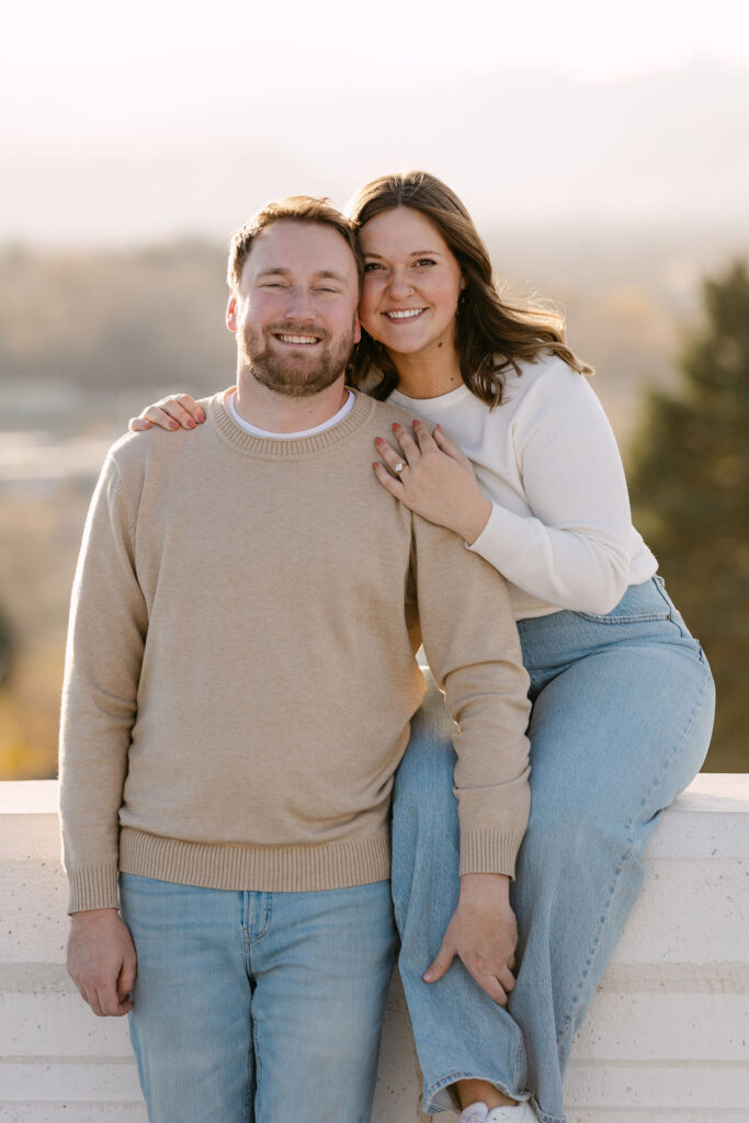 Couple smiling together while sitting on the overlook wall at Inspiration Point Park in Denver