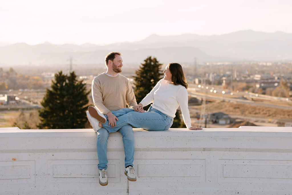 Couple sitting at Inspiration Point Park in Denver with mountains in the background during their engagement session