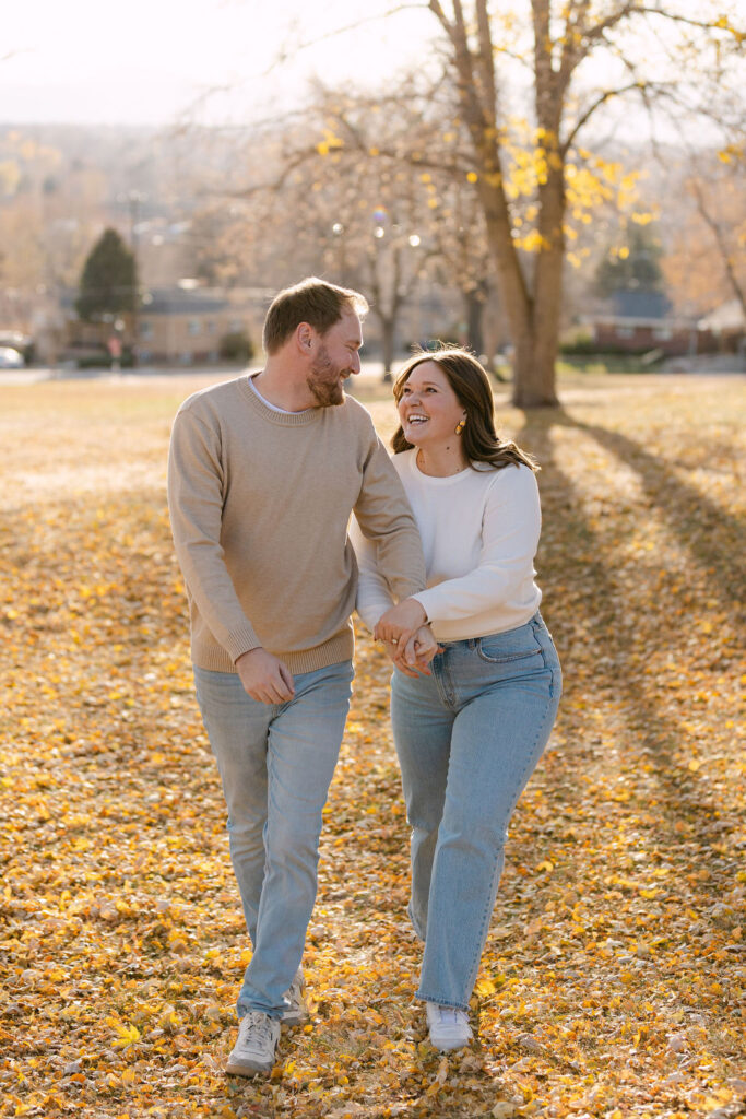 Couple walking hand in hand through leaves during their Denver engagement session