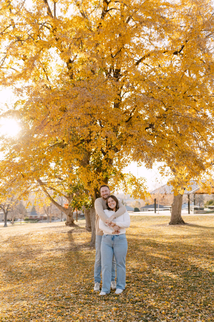 Wide shot of couple under a tall yellow tree during fall engagement photos in Denver.