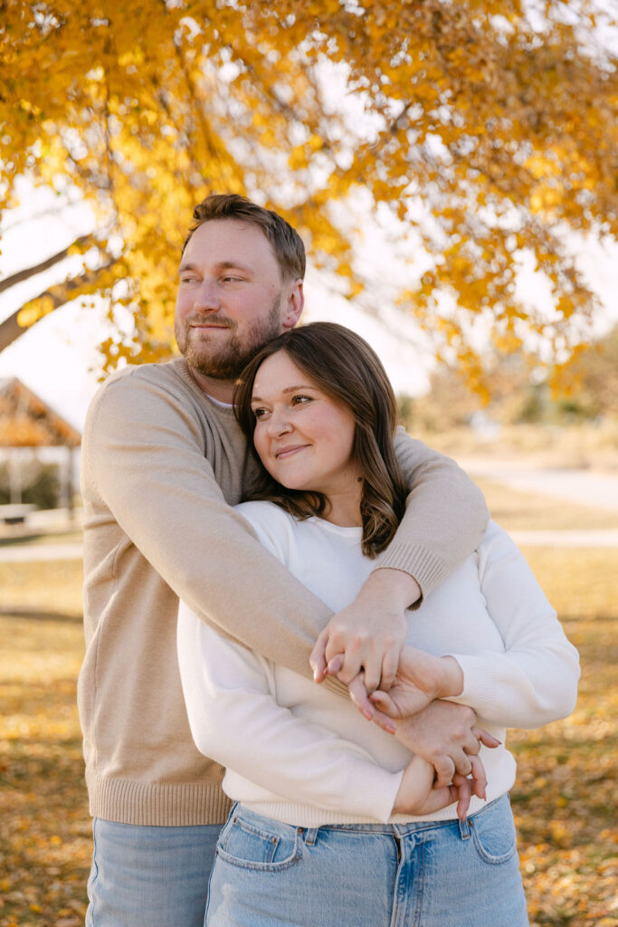 Couple hugging beneath a bright yellow fall tree during their Denver engagement photos.