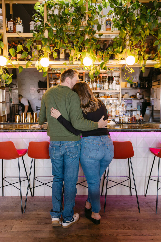 Couple hugging while ordering their drinks at a colorful cocktail bar in Denver during their engagement session 