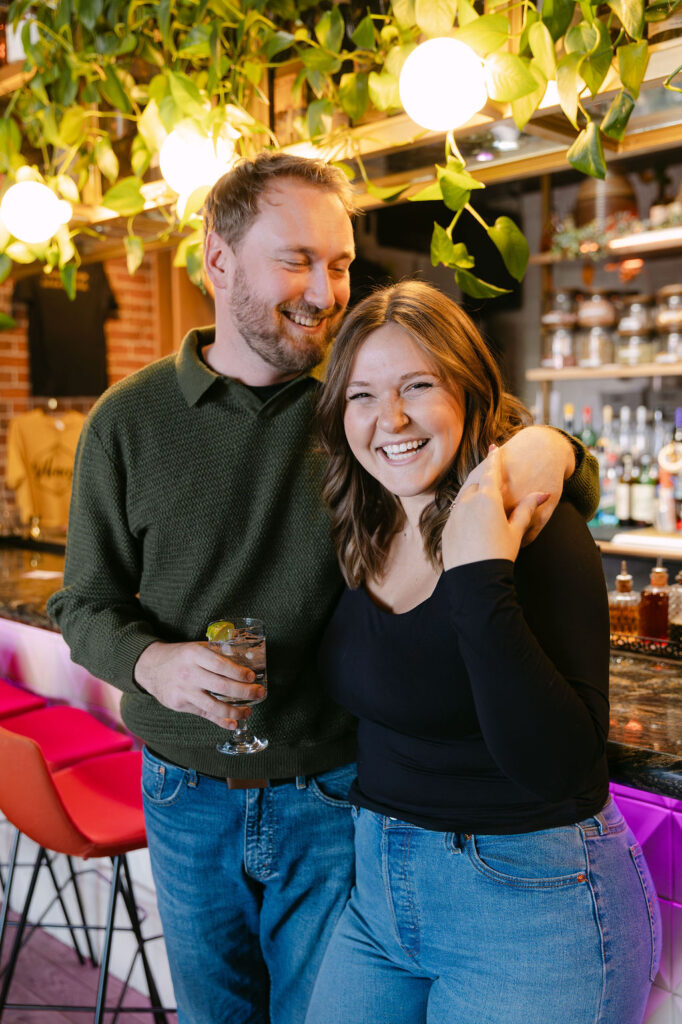 Natural engagement photo of a woman laughing at the camera while her fiance gives her kisses 