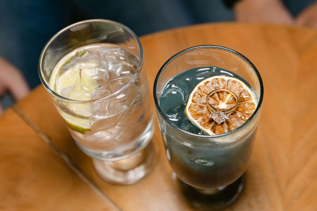 Creative engagement photo with the woman's engagement ring floating on top of dried fruit in her cocktail at a cocktail bar in Denver