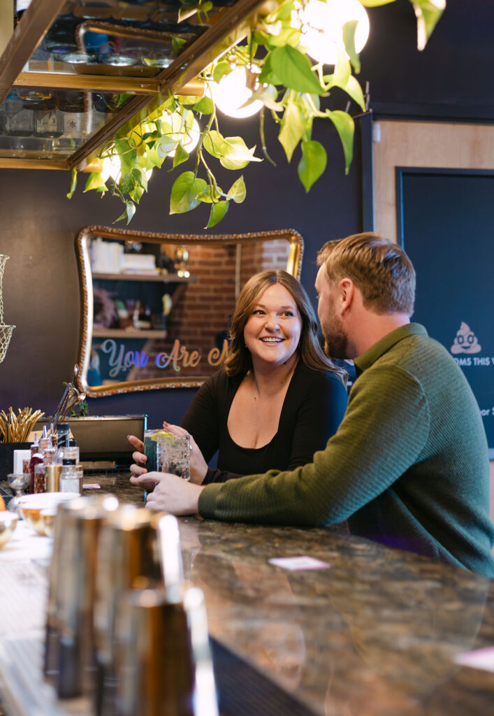 Candid engagement photo of a woman lovingly smiling at her fiance while sitting at a cocktail bar in Denver 
