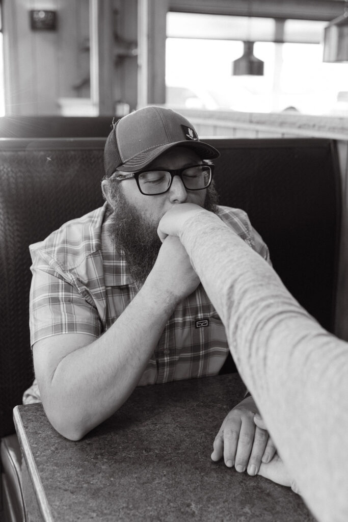 Black and white photo of groom-to-be kissing his partner’s hand during their nostalgic diner engagement session