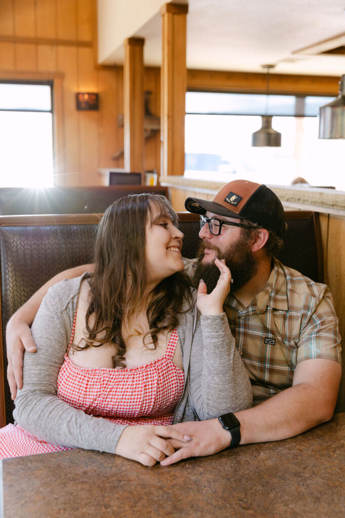 Couple sitting in a booth at Vern’s Place during their Northern Colorado diner engagement session, smiling and leaning into each other.