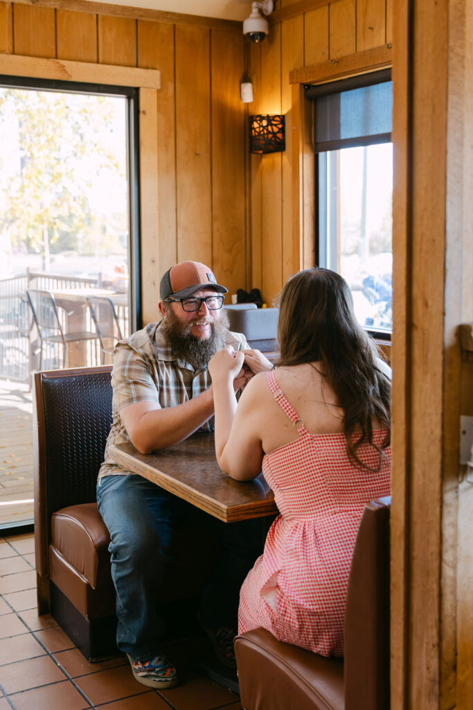 Couple holding hands across a diner table at Vern’s Place during their Colorado engagement photos.