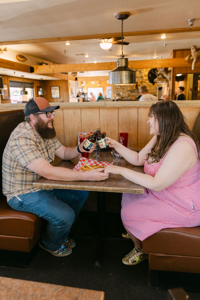 Couple cheersing Coors beers together in a Vern’s booth during their Northern Colorado engagement photos.