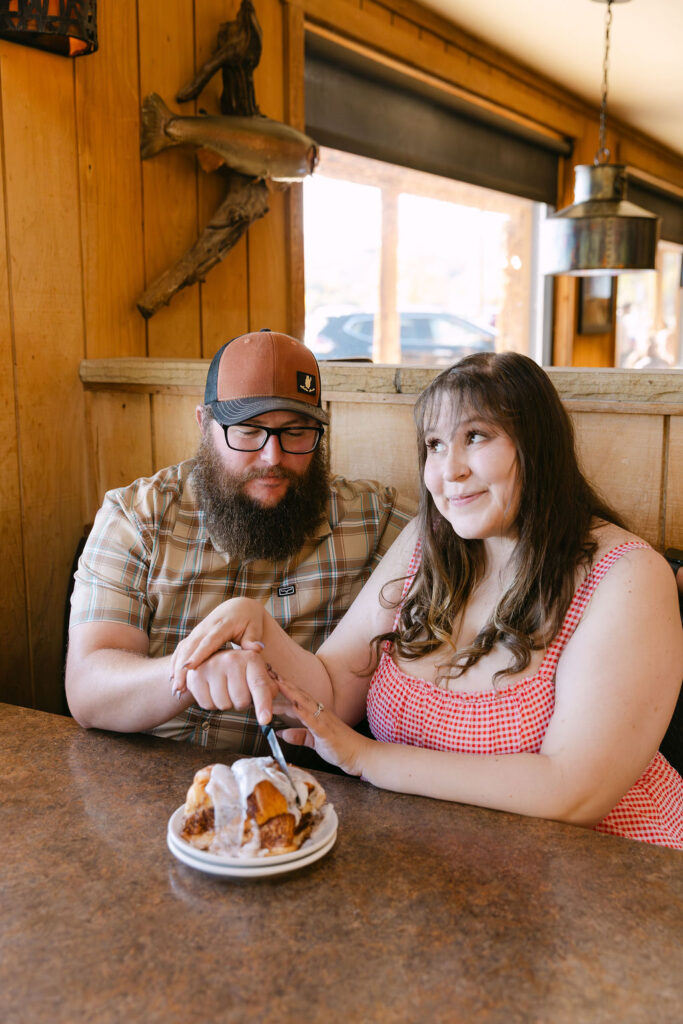 Couple posing with cinnamon roll dessert during their cozy Vern’s diner engagement session.