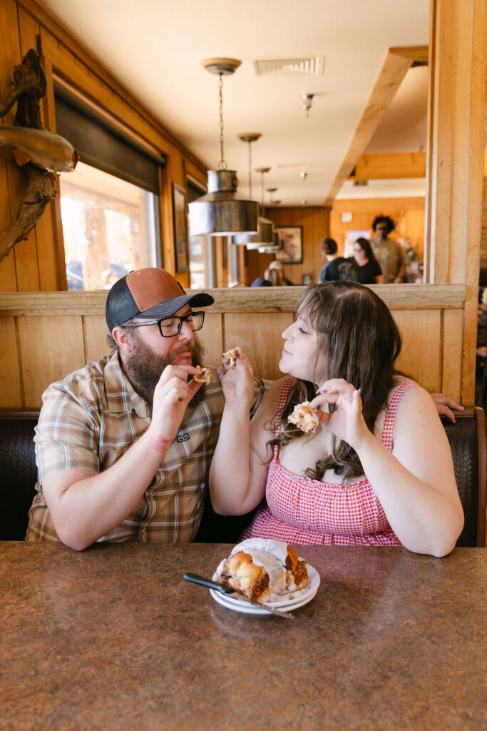 Couple sharing a cinnamon roll together at Vern’s Place during their nostalgic diner engagement session