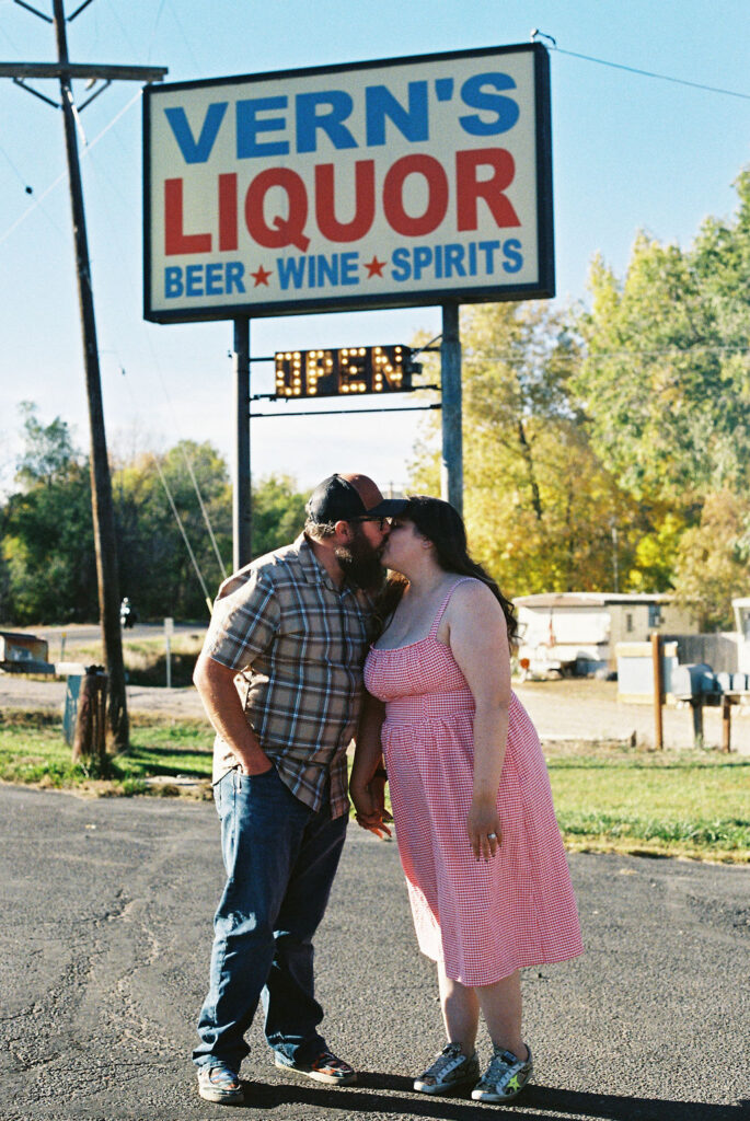 Couple kissing beneath the Vern’s Liquor sign near Vern’s Place during their diner engagement photos.