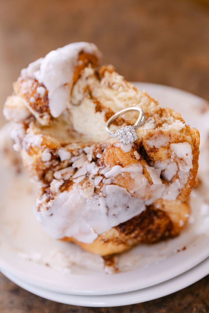 Cinnamon roll topped with icing and an engagement ring during Vern’s Place diner engagement photos in Northern Colorado.