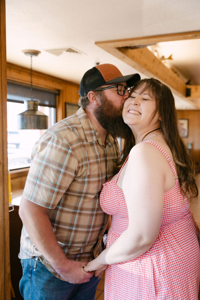 Partner kissing the bride-to-be’s cheek inside Vern’s Place during their Colorado engagement session.