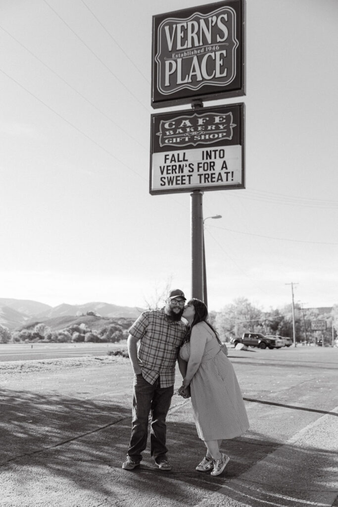 Black and white photo of couple kissing under the Vern’s Place sign during their Colorado engagement session