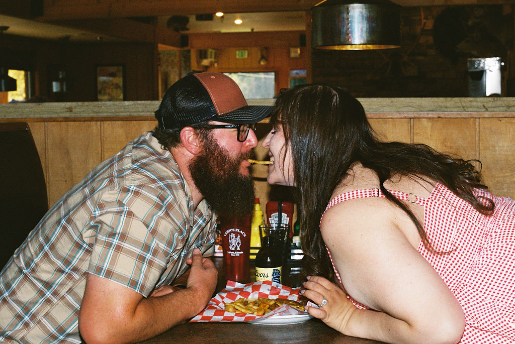 Couple leaning across the booth pretending to share a fry Lady-and-the-Tramp style during their diner engagement session