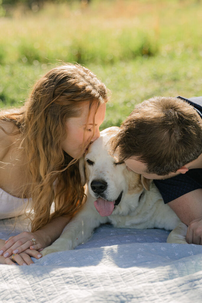 Annelise and Ross kissing their dog while laying on a blanket during their engagement photos in Fort Collins 