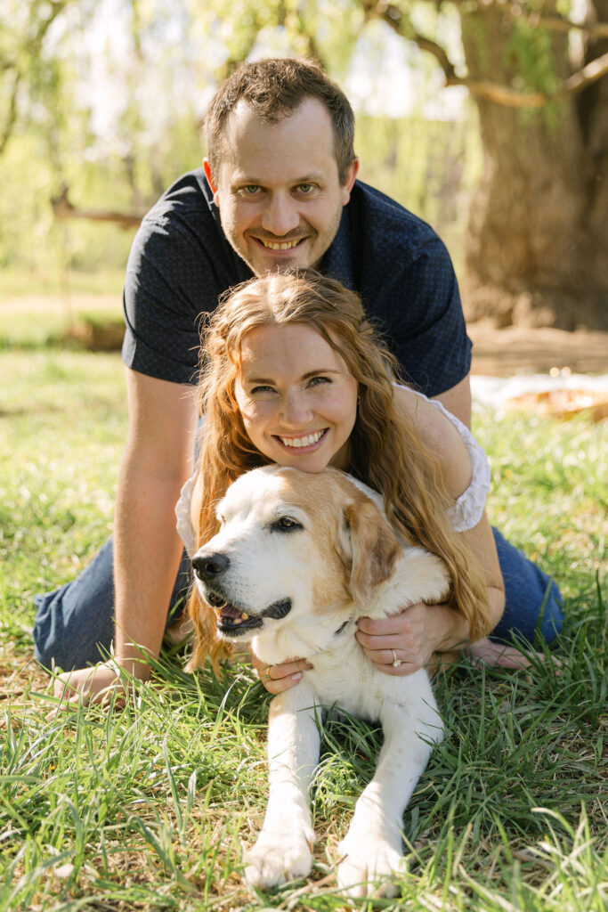 Annelise and Ross cuddling with their dog, Professor, during their picnic engagement session in Fort Collins.